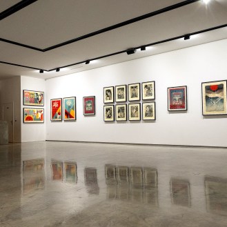 A modern art gallery with white walls displaying framed art prints. A person in light clothing stands near a counter on the…