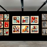 A modern art gallery with a black wall displaying two grids of framed art prints. The left grid features colorful portraits…