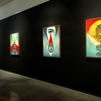 A modern art gallery with a black wall displaying four framed art prints. The prints feature colorful designs, including a…