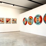 A modern art gallery with four circular mandala-patterned artworks on a white wall. To the left, four framed art prints with…
