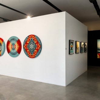 A modern art gallery with four circular mandala-patterned artworks on a white wall. To the right, a dark hallway leads to a…