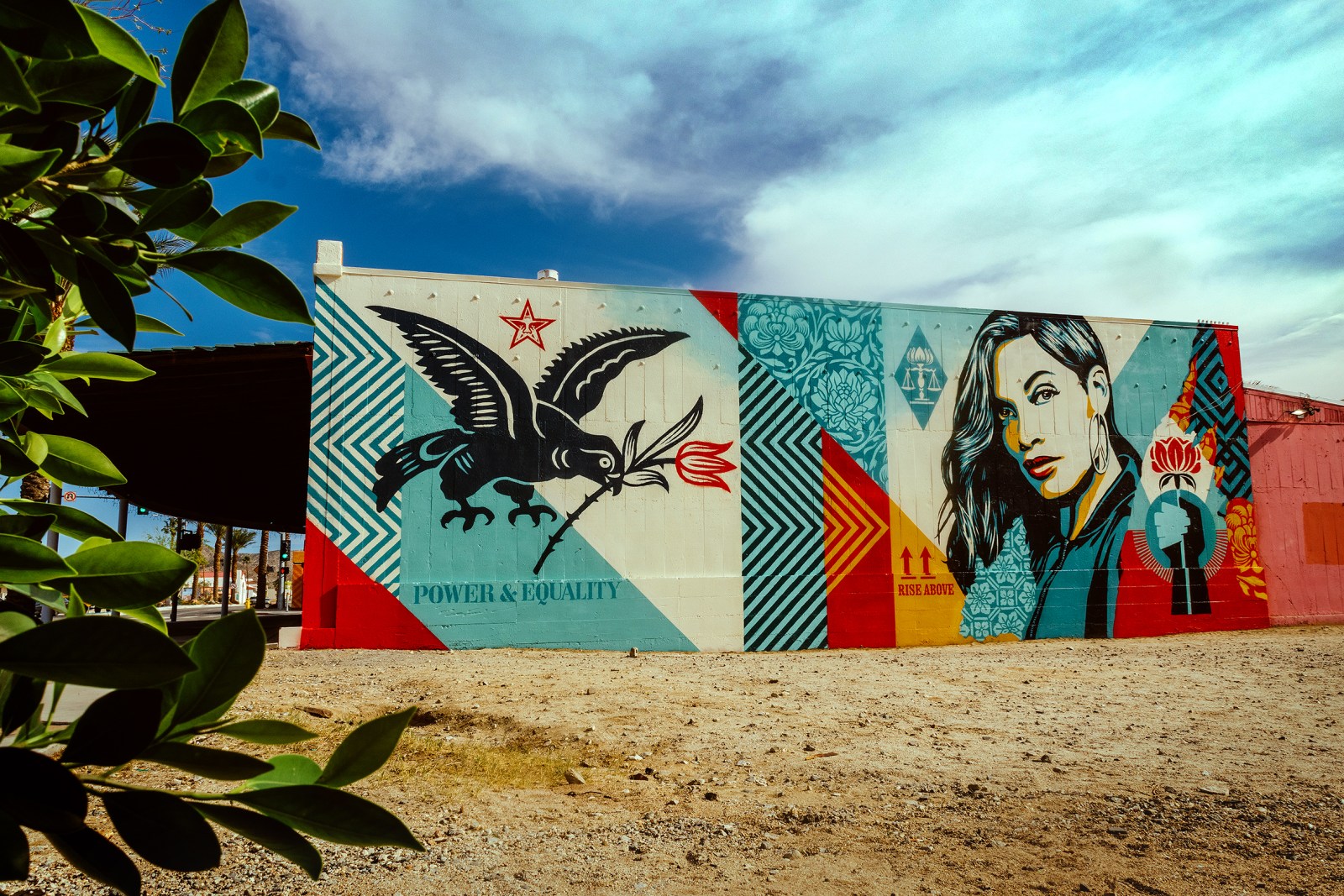 A colorful mural on a building featuring a bird, a woman's portrait, and various patterns in red, blue, yellow, and cream&hellip;