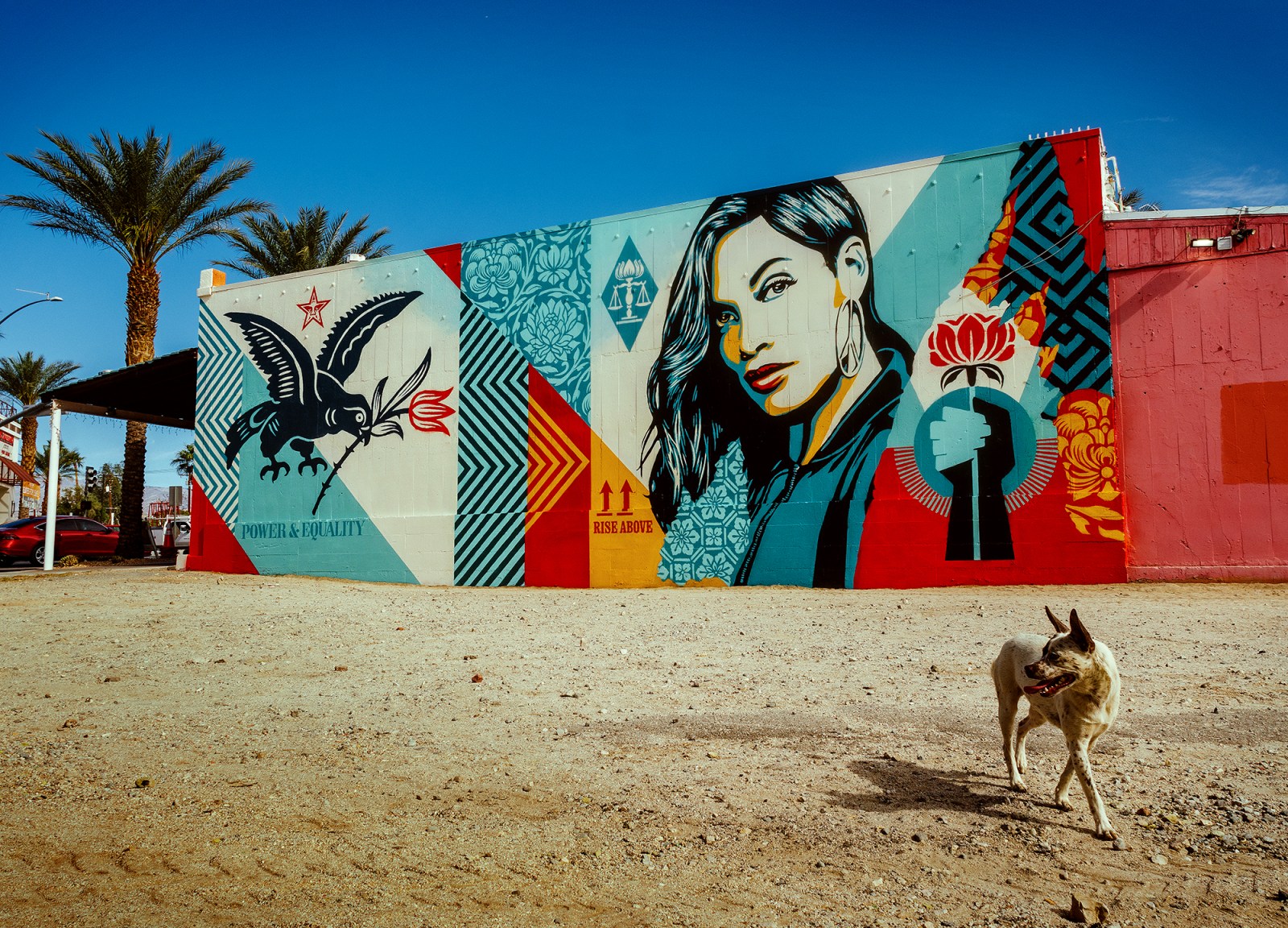 A colorful mural on a building featuring a bird, a woman's portrait, and various patterns in red, blue, yellow, and cream&hellip;