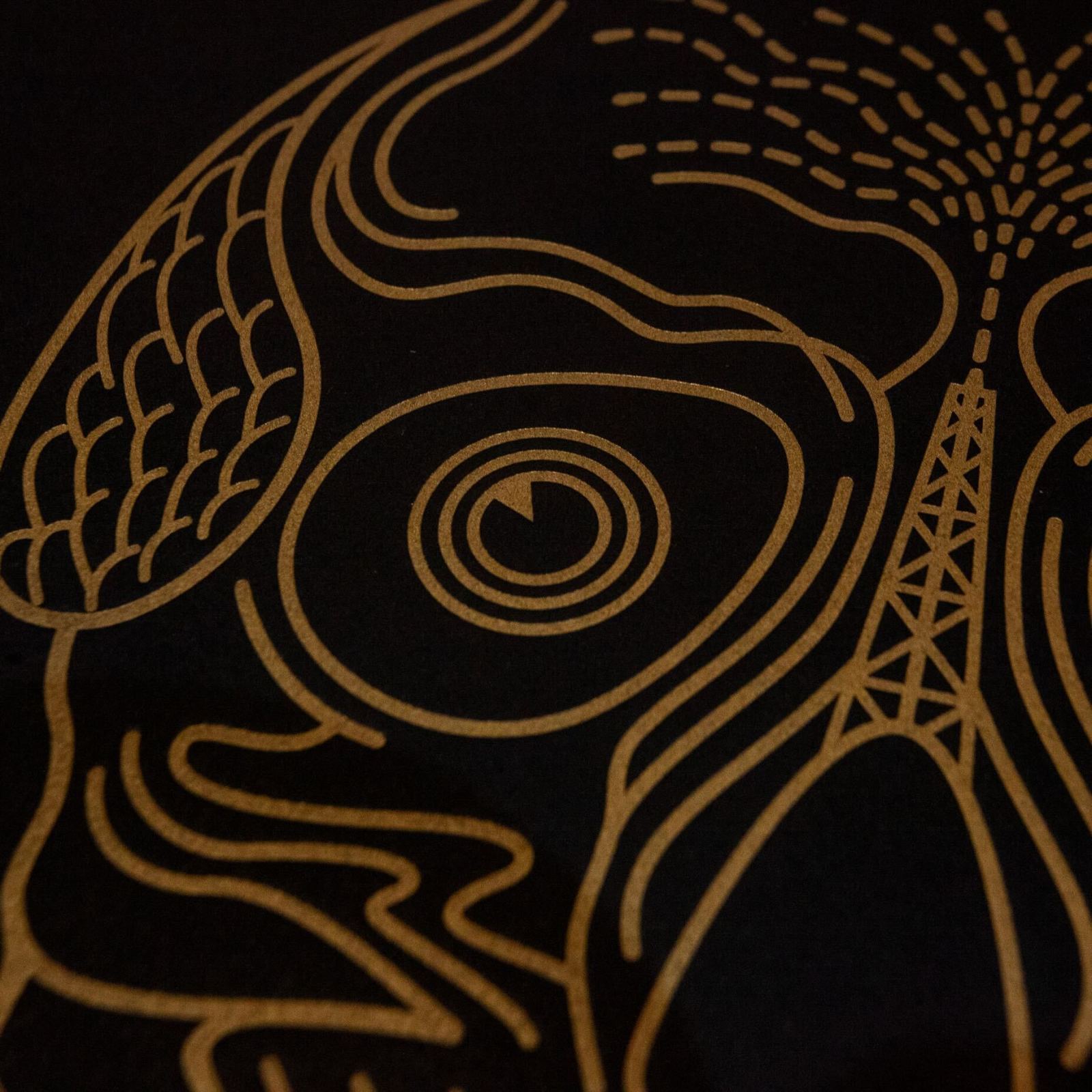 Gold line art on black fabric depicting a stylized skull with an oil derrick.