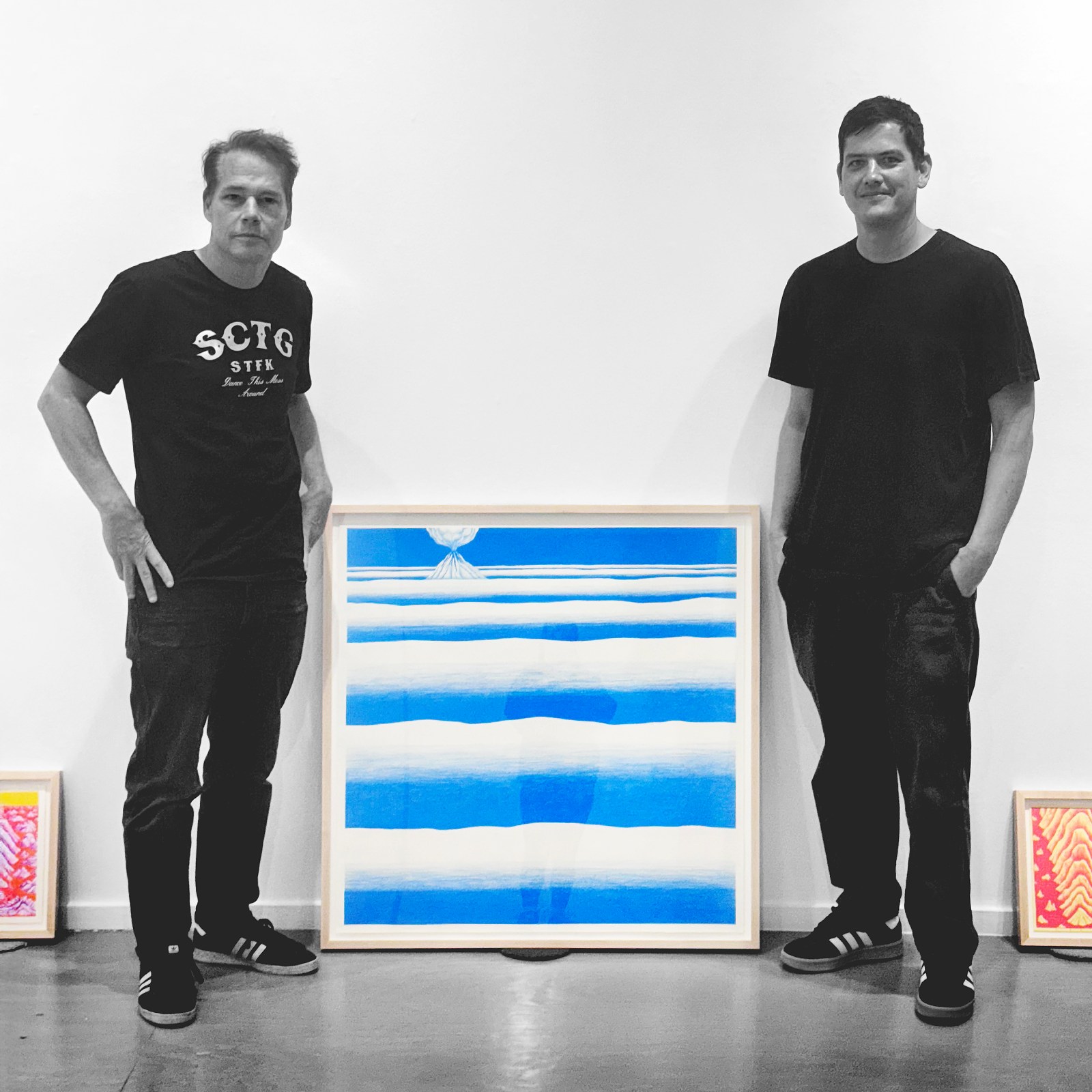 Two men stand on either side of a framed artwork featuring blue and white horizontal stripes with a small white dome at the&hellip;