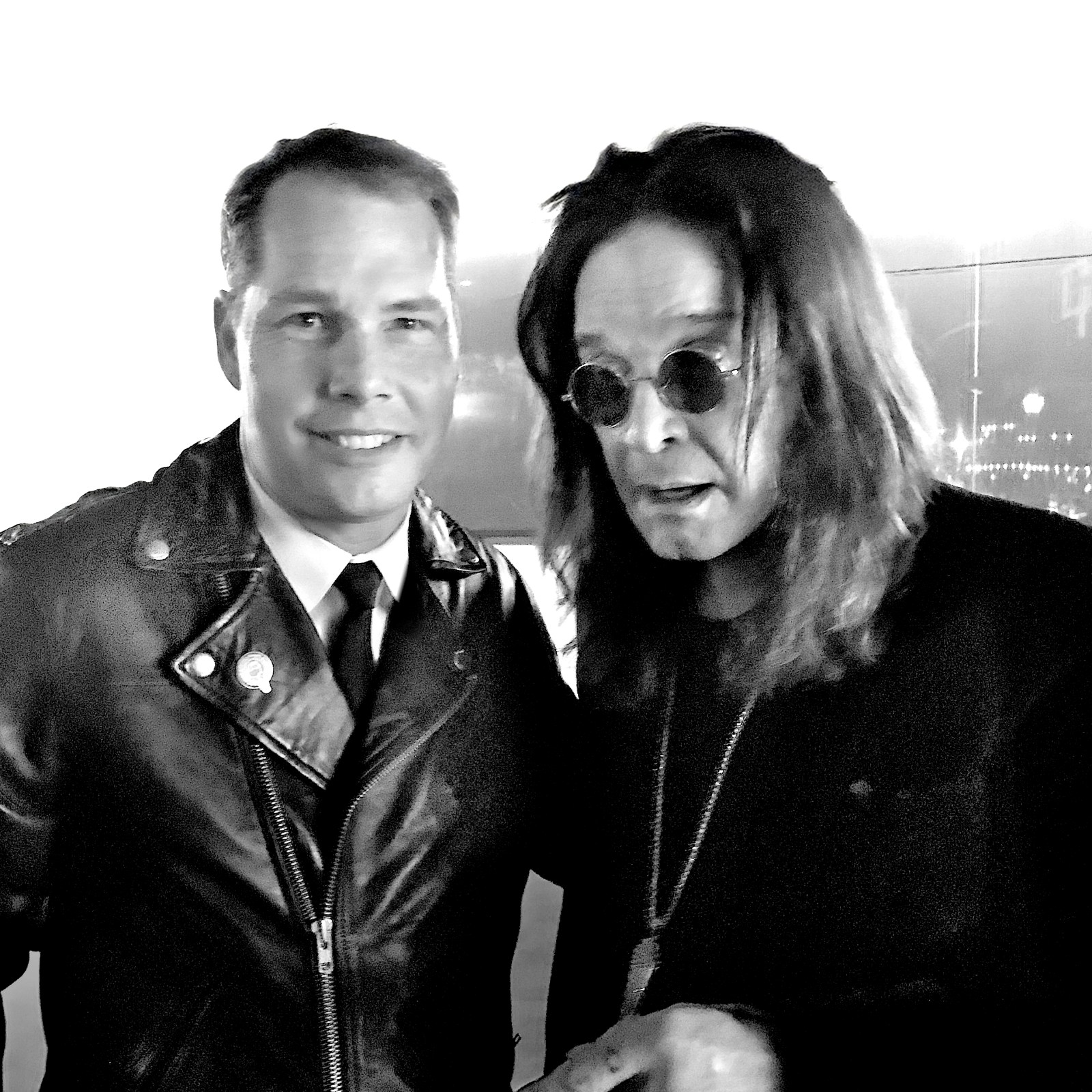 Black and white photo of two men; one in a leather jacket, the other with long hair and sunglasses.