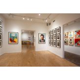 Art gallery with light wood floors, white walls, and various framed artworks, including a large portrait of Muhammad Ali.