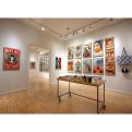Art gallery with light wood floors, white walls, and a large collection of framed artworks, including a red "MAKE ART NOT…