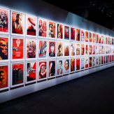 A long gallery wall filled with a grid of numerous framed pop art posters in red, white, and black, featuring various…
