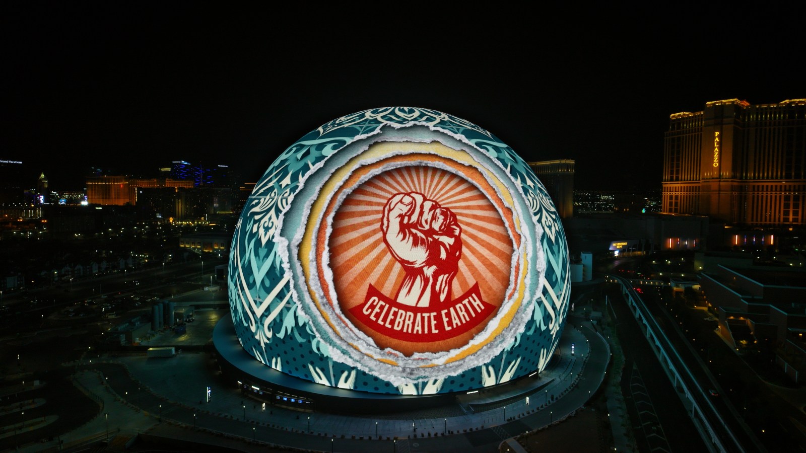 An aerial view of a large spherical building illuminated with a red raised fist and the text