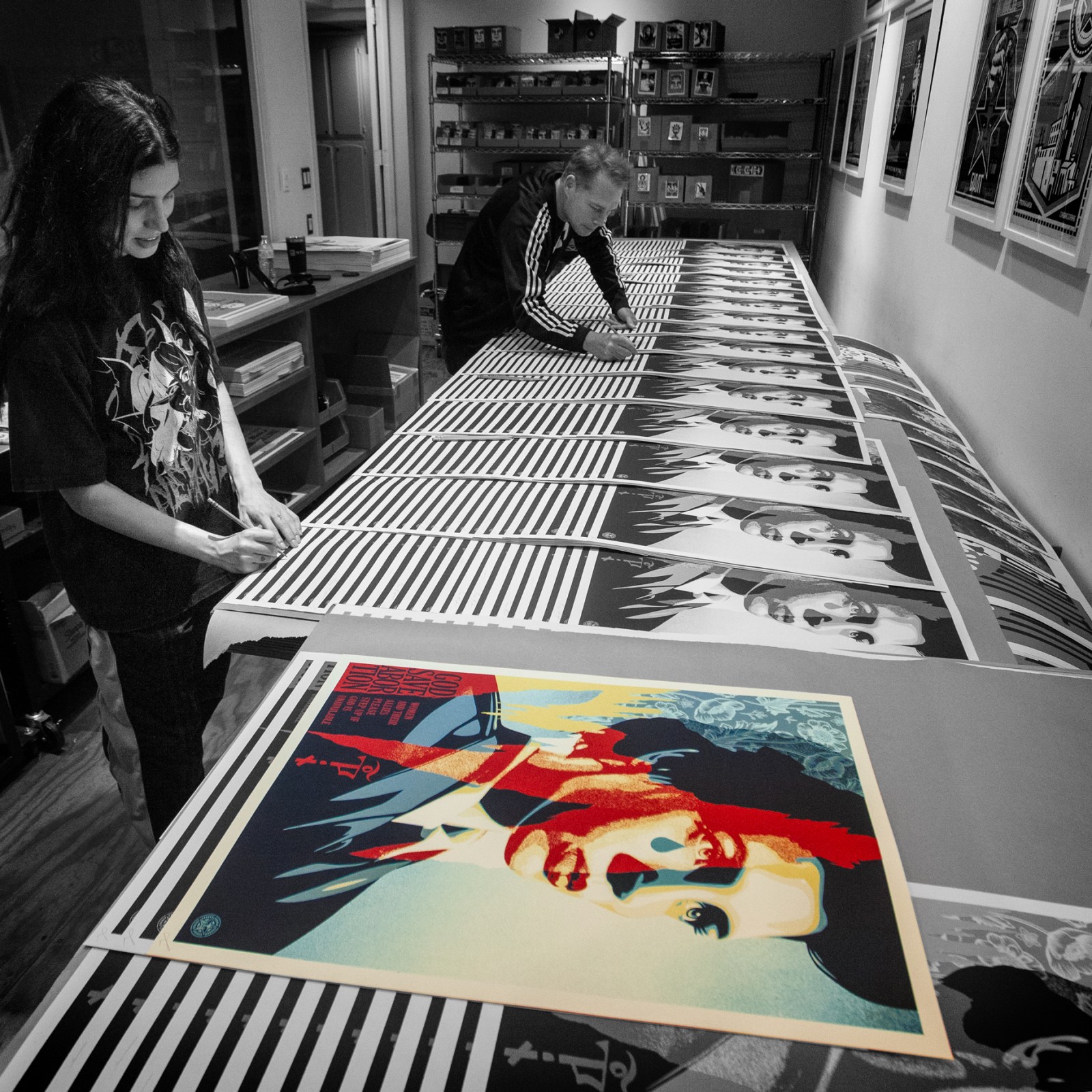 A man and woman in a studio, surrounded by prints of a woman's face, with one print in the foreground.