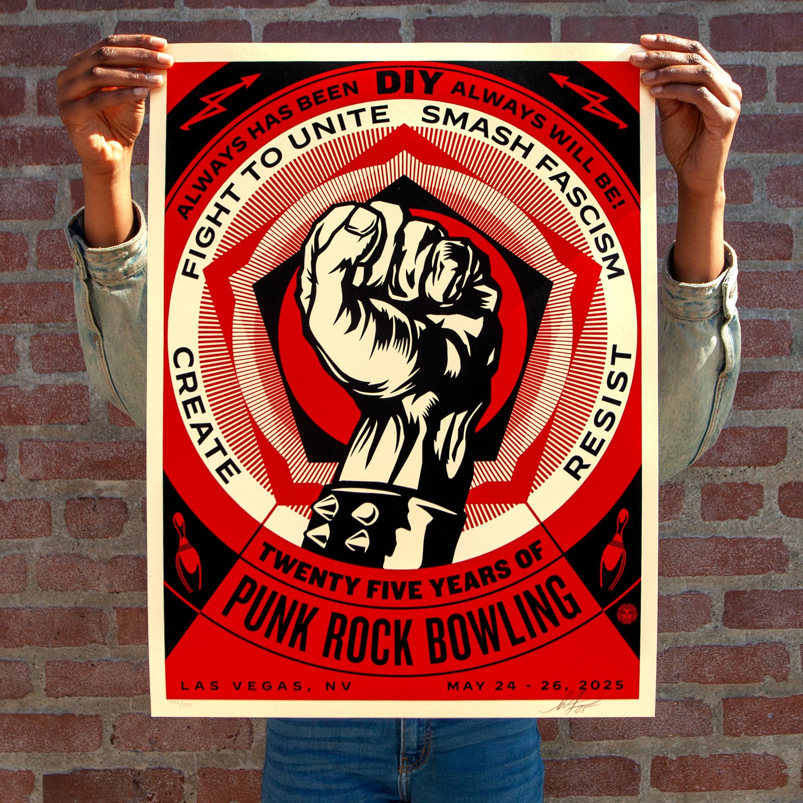 A person holds a red, black, and white poster with a raised fist in the center, surrounded by text: "ALWAYS HAS BEEN DIY&hellip;