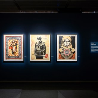 A dark blue gallery wall with three framed art prints. The first shows a couple, the second a man in a helmet, and the third…